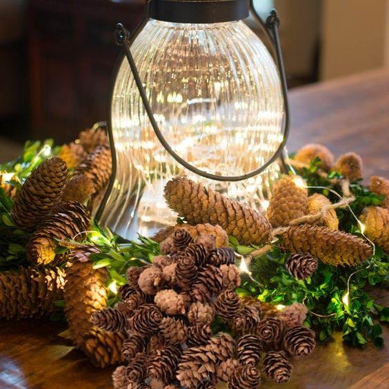 Assortment of natural pine cones arranged around a decorative lantern with fairy lights