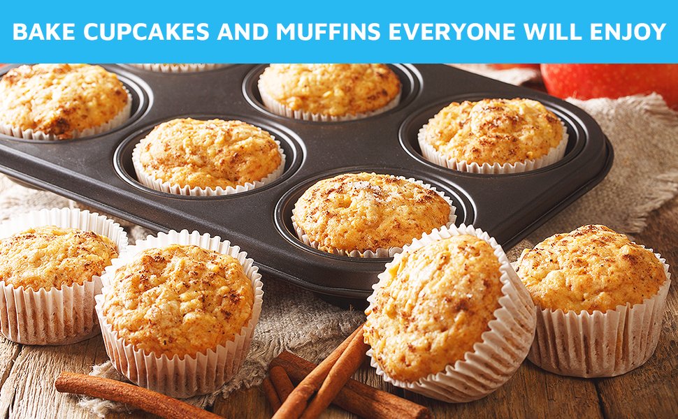 Muffins baked in white paper liners in a muffin tin, with cinnamon sticks on a wooden surface.