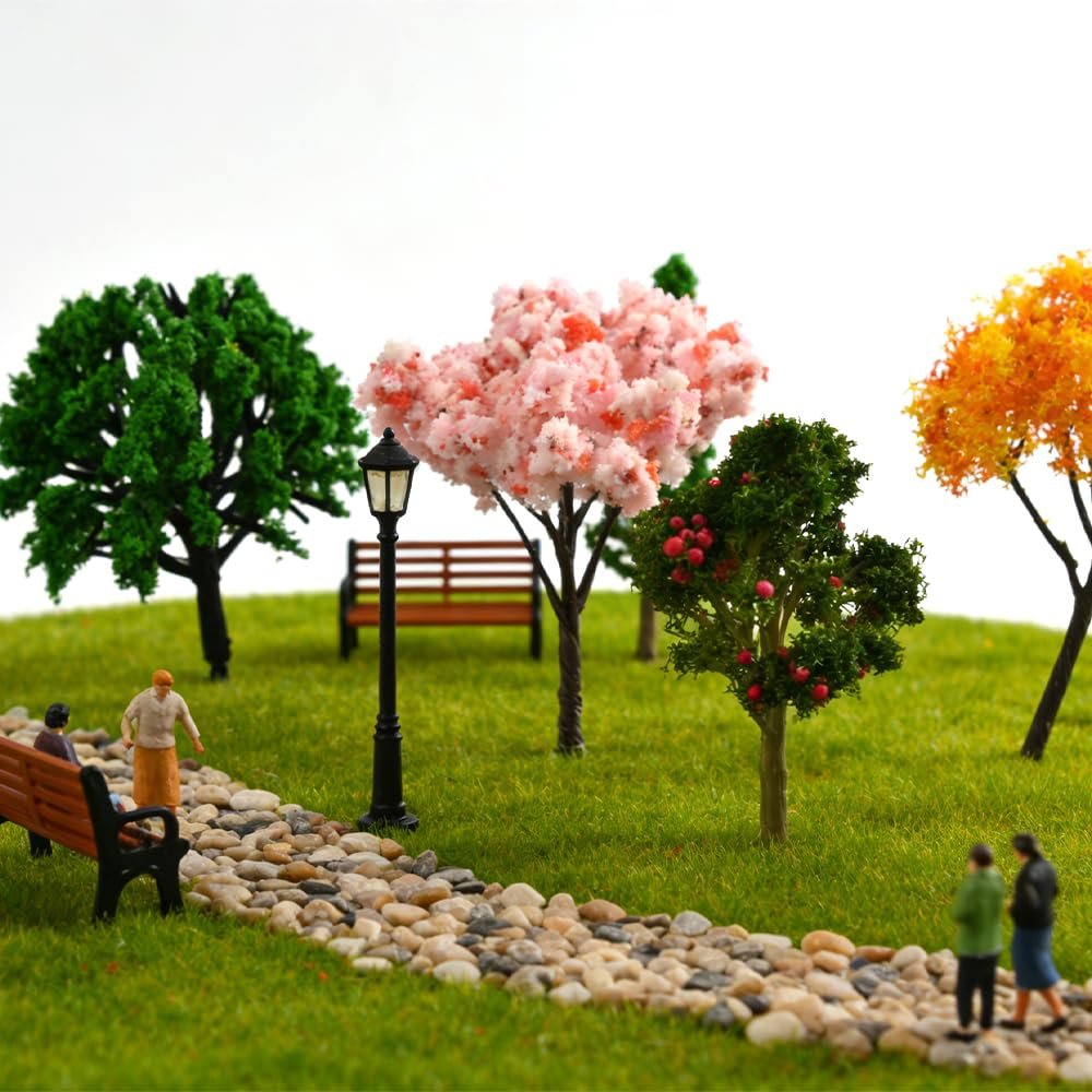 Miniature park scene with diverse artificial trees, benches, lamppost, and tiny figures on a grassy knoll.