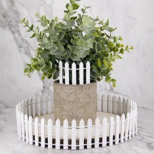 Miniature white picket fence arranged around a potted plant and on a wooden slice