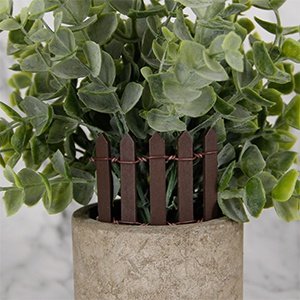 Miniature brown wood picket fence section with wire detail inserted into a faux plant in a concrete pot.
