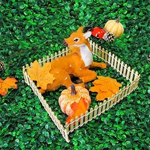Miniature wood picket fence enclosing a deer, pumpkins, and autumn leaves on a green background.