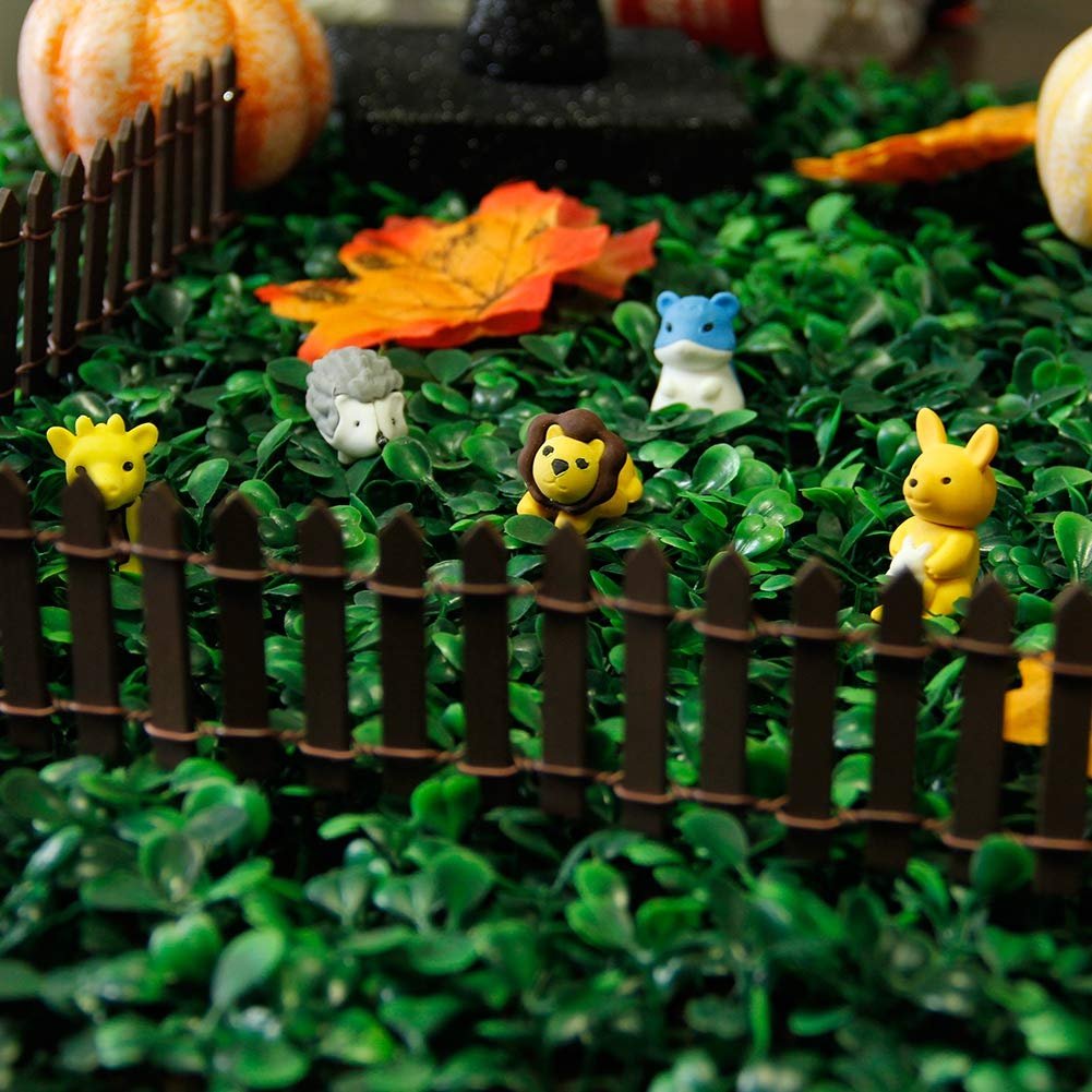 Miniature brown picket fence with small animal figurines in a fairy garden setting with artificial greenery and pumpkins.