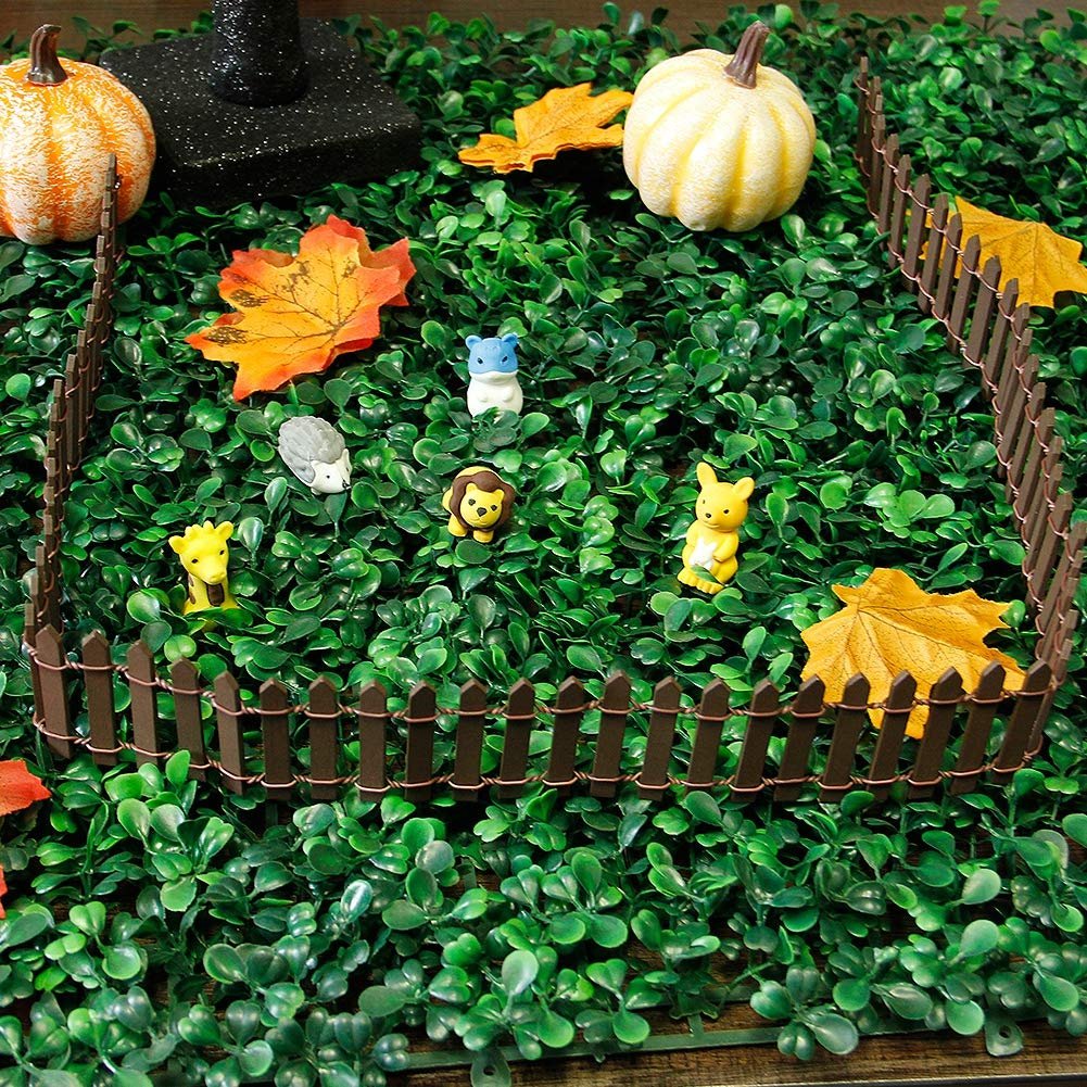 Miniature brown picket fence enclosing small animal figurines on artificial green foliage with pumpkins and autumn leaves.