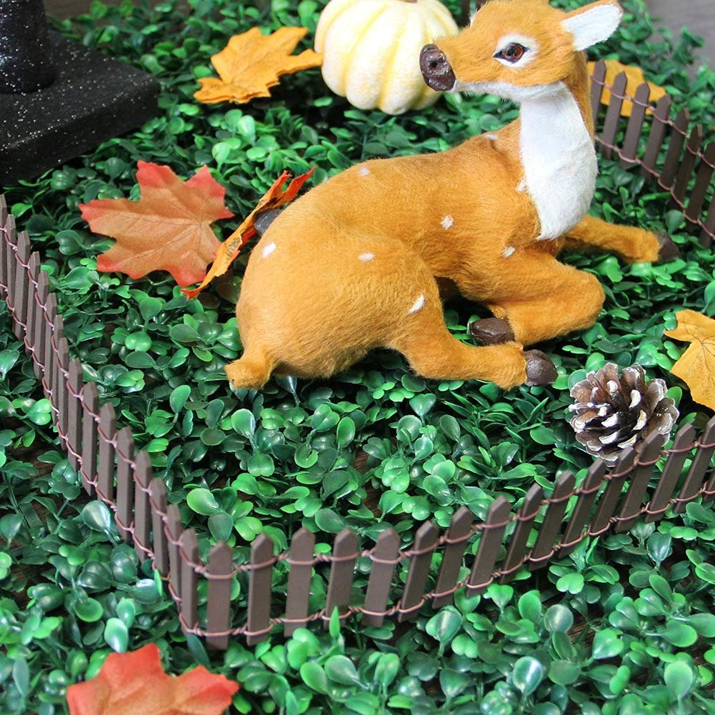 Miniature brown picket fence section surrounding a fuzzy deer figurine on artificial green grass with autumn leaves and a small pumpkin