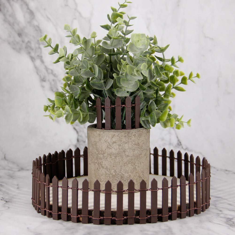 Miniature brown wood picket fence encircling a potted plant on a marble surface