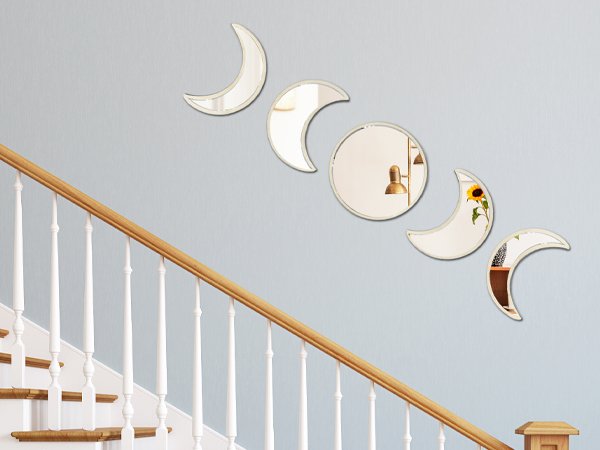 Five moon phase acrylic mirrors arranged on a light blue wall above a wooden staircase railing.