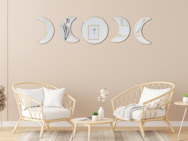 Five moon phase acrylic mirrors arranged on a wall above two rattan chairs and a coffee table.