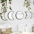 Five moon phase mirrors arranged on a white wall above a sofa with decorative pillows and a throw blanket.