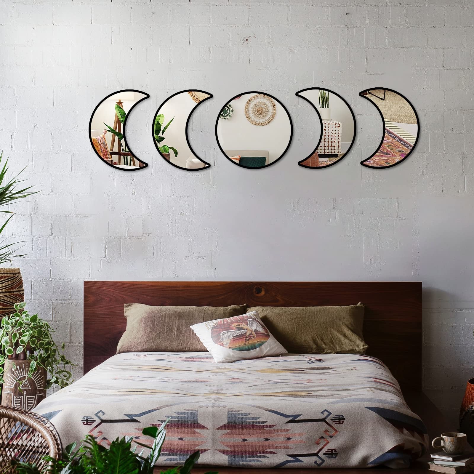 Five moon phase acrylic mirrors mounted on a white brick wall above a bed with boho-style bedding.