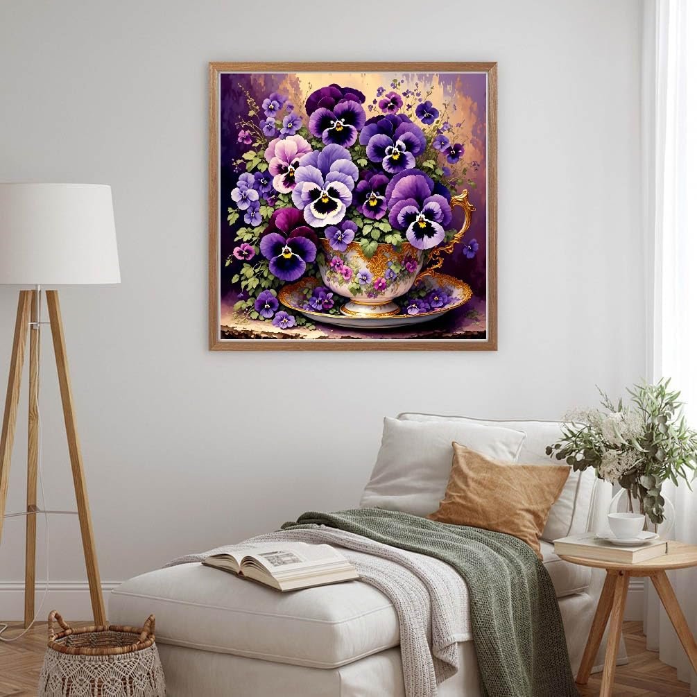 Diamond painting kit featuring a teacup overflowing with purple and pink pansies, displayed in a living room setting.