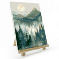 Paint by number canvas showing a mountain landscape with a sun and pine trees, displayed on a wooden easel.