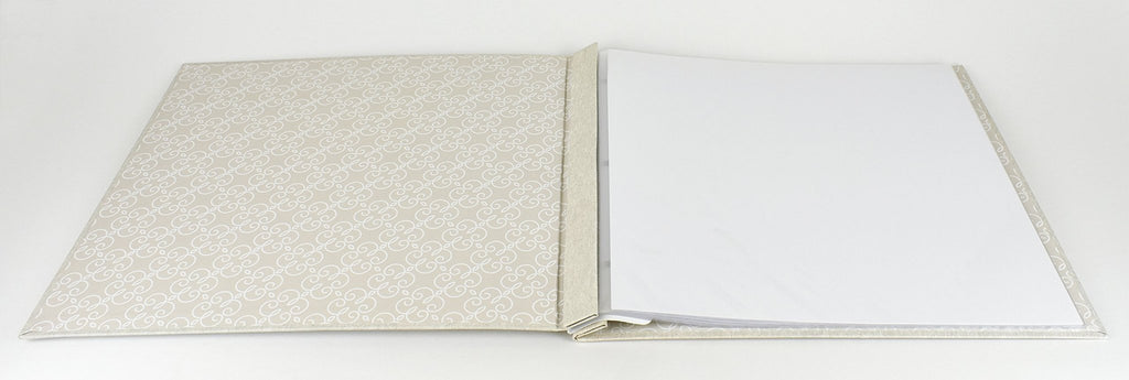 Open ivory post-bound scrapbook album with decorative pattern on the left cover and blank pages on the right.