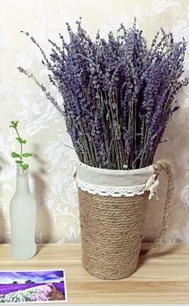 Dried lavender bouquet in a decorative rope vase next to a frosted glass bottle with a sprig of greenery.