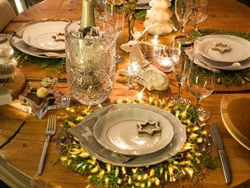 Festively set dining table with place settings, champagne bucket, and holiday decorations.