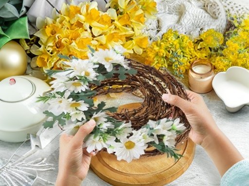 Hands holding a grapevine twig wreath decorated with white daisies and green leaves, surrounded by craft supplies and spring flowers.