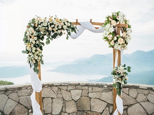 Wedding arch decorated with flowers and draped fabric, set against a scenic mountain and water backdrop.