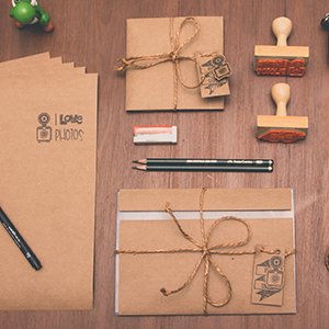 Flat lay of craft supplies including envelopes, twine, stamps, pencils, and a small green figurine on a wooden surface.