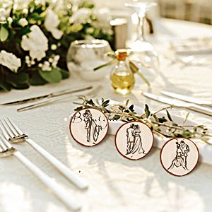 Three unfinished wooden circles with wedding couple illustrations, set on a table with cutlery and floral decor.