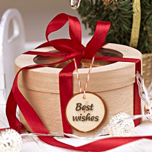 Round wooden gift box with red ribbon and a wooden slice tag that says 'Best wishes', next to a Christmas tree.