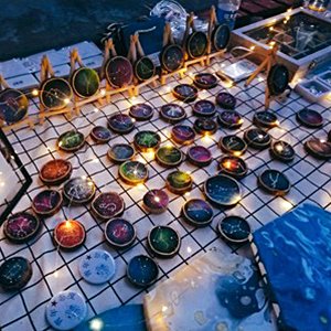 Collection of decorated wooden slices with celestial designs displayed on a checkered cloth with fairy lights.