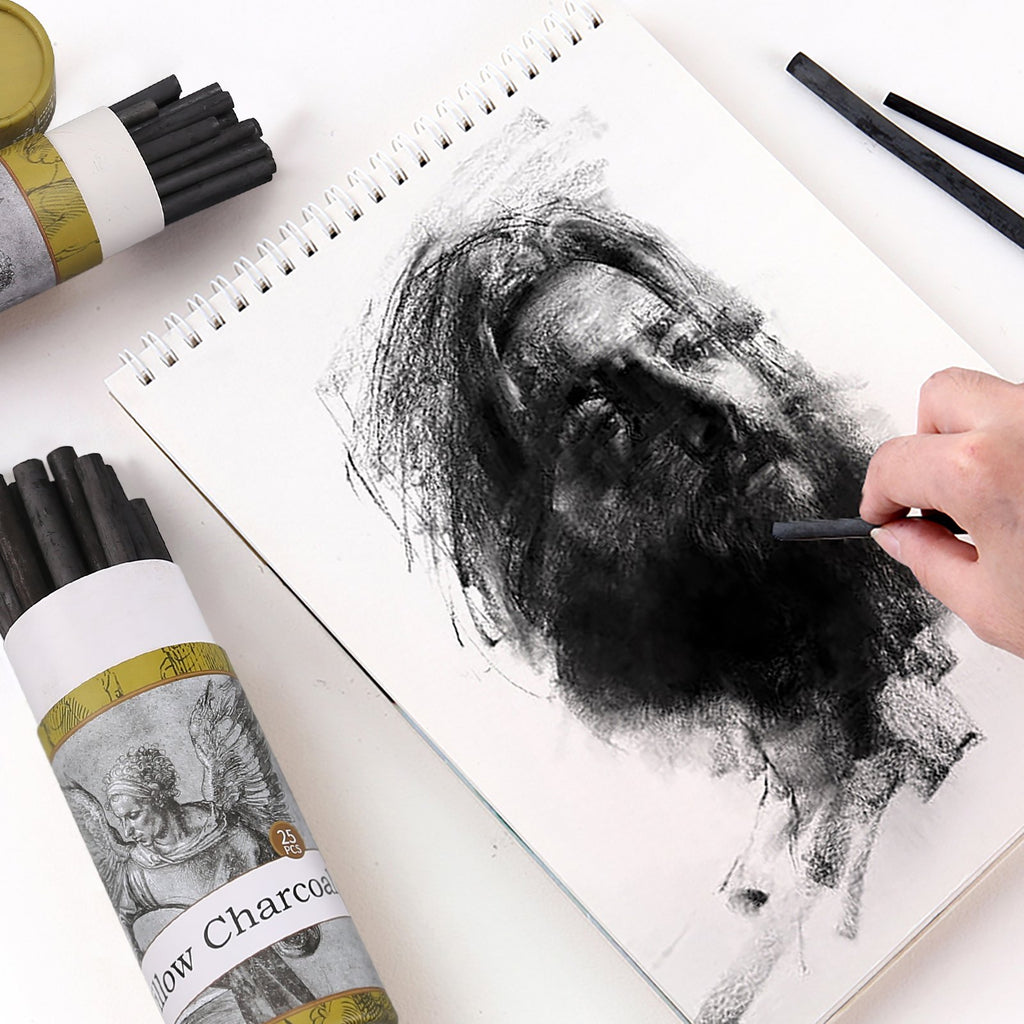 Artist sketching a portrait with willow charcoal sticks on a spiral-bound sketchbook page, with charcoal tubes in foreground.