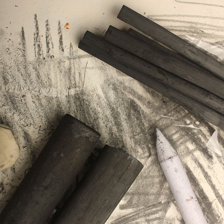 Several charcoal drawing sticks and a blending stump on a surface with charcoal sketches.