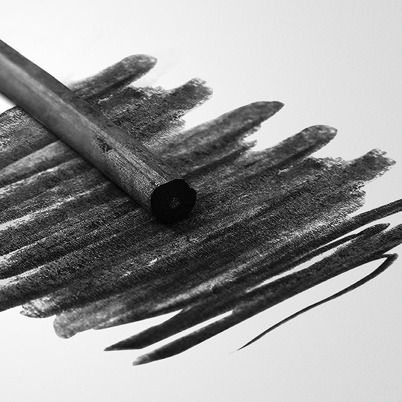 Willow charcoal stick creating dark smudges on white paper, close-up angle