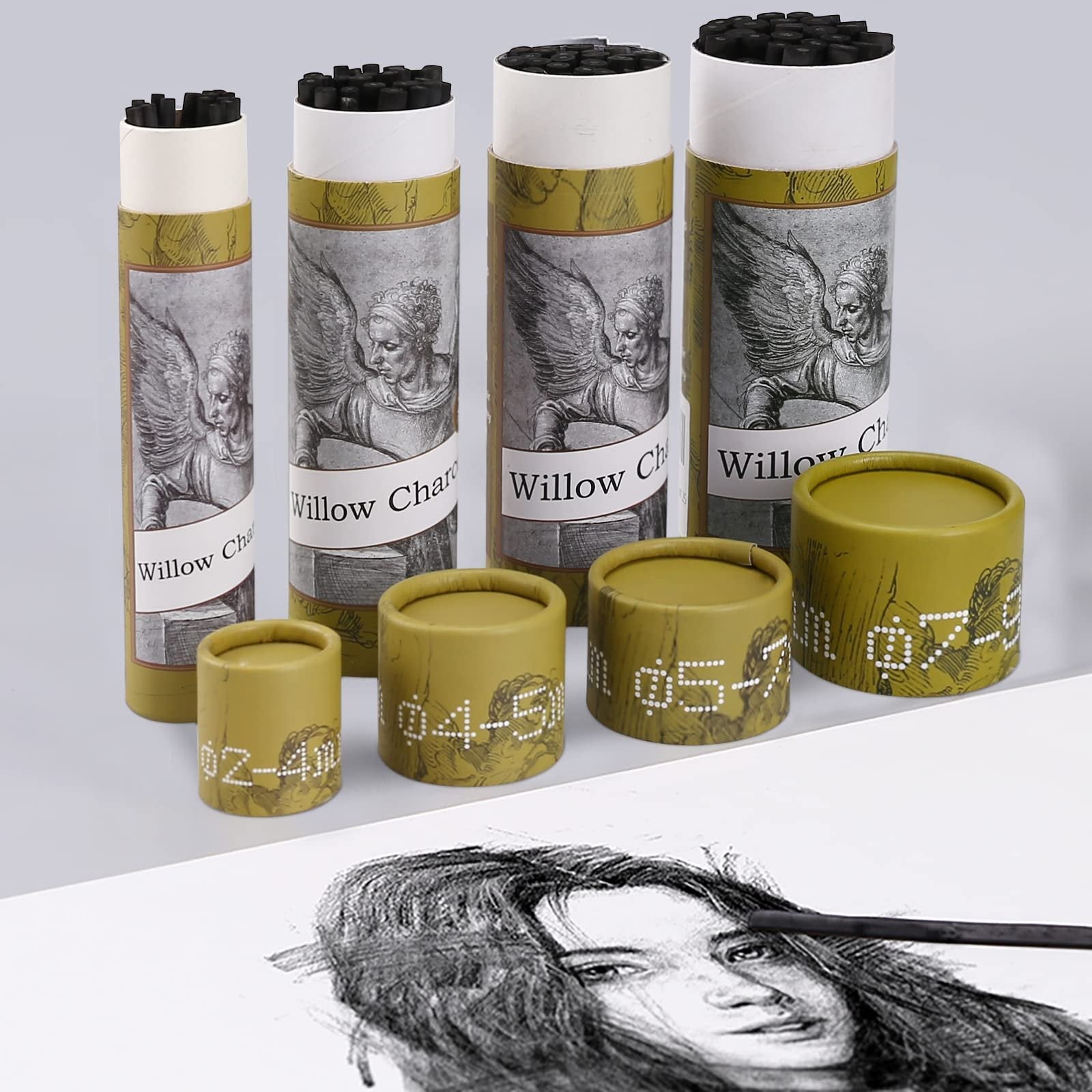 Assortment of willow charcoal sticks in cylindrical packaging with artistic designs, alongside a sketch of a face with a charcoal stick.