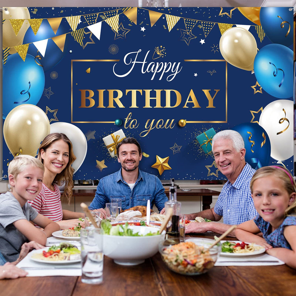 Family celebrating a birthday at a dinner table with a navy blue and gold backdrop featuring balloons and banners.