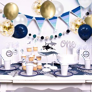 Party table setting with navy blue, gold, and pearl white balloons, cupcakes, and whale decorations.