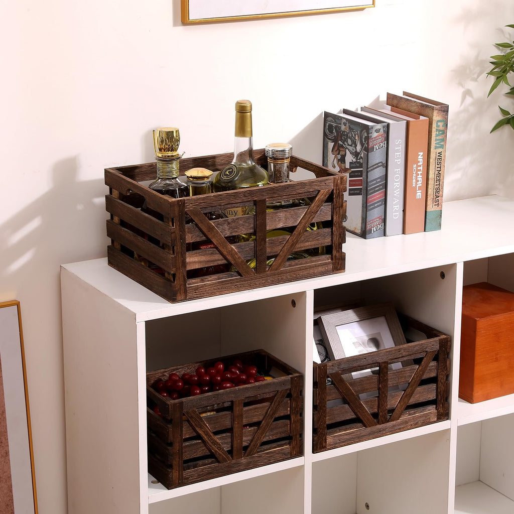 Three wooden storage crates with handles, one filled with bottles and jars, another with grapes, and the third with a picture frame, displayed on white shelving.