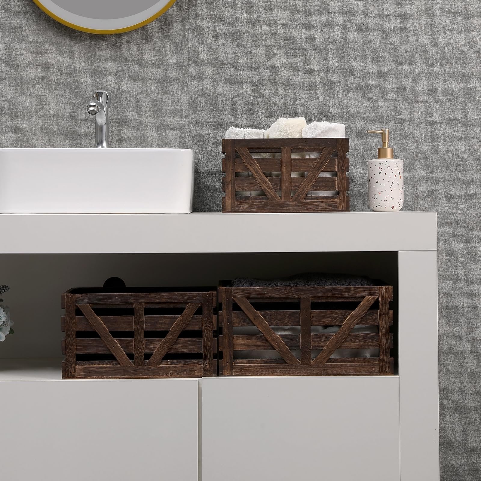 Three dark wood decorative storage crates with handles on a white vanity, two filled with towels.