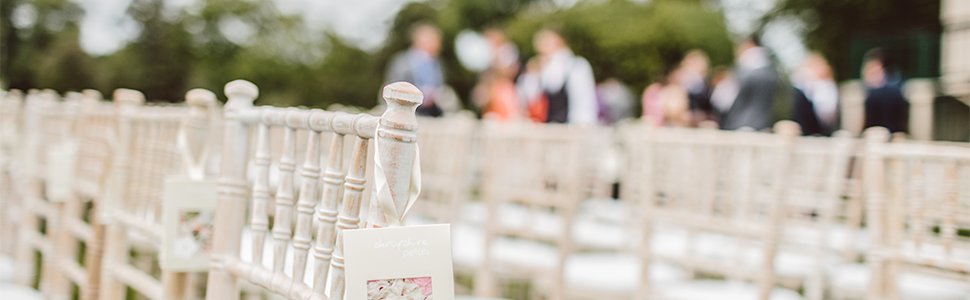 Wedding ceremony seating with programs attached to chairs, guests blurred in background