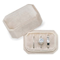 Beige velvet ring box with three slots holding engagement ring, wedding band, and diamond band.