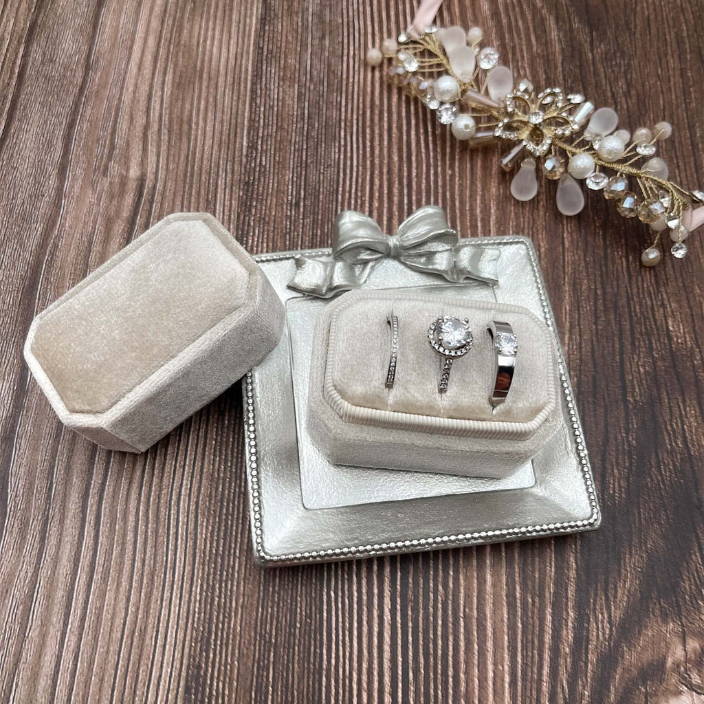 Velvet ring box with three slots holding engagement rings and wedding bands, next to an open ring box.