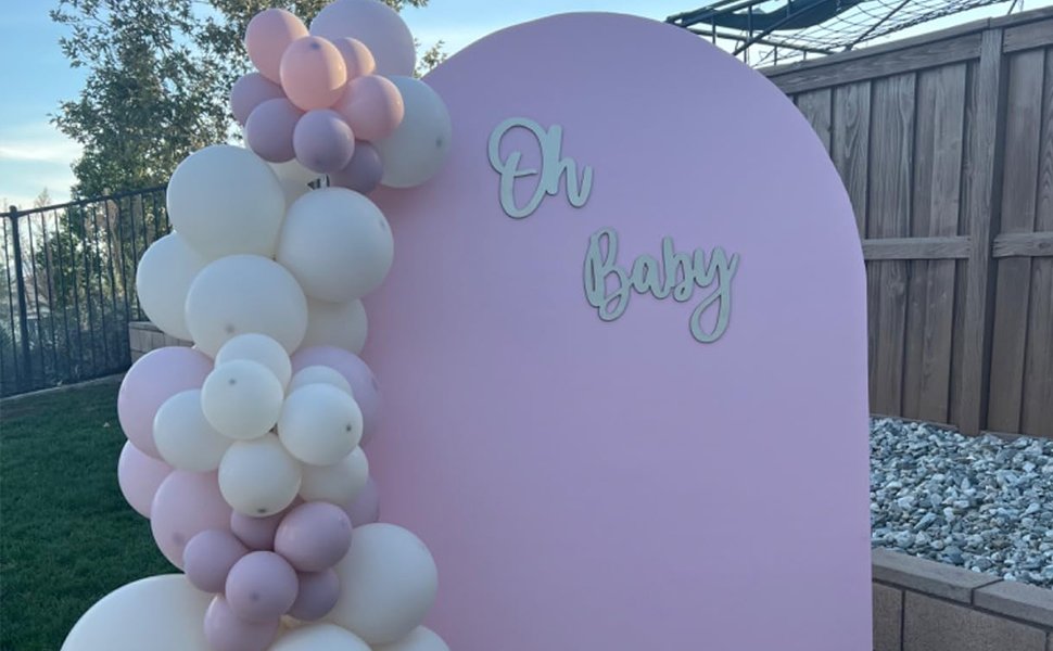 Pink arch backdrop with a balloon garland and 'Oh Baby' wooden cutouts for a baby shower or gender reveal.