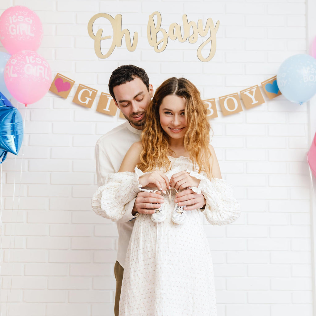 Couple holding baby booties with 'Oh Baby' sign and balloons for baby shower