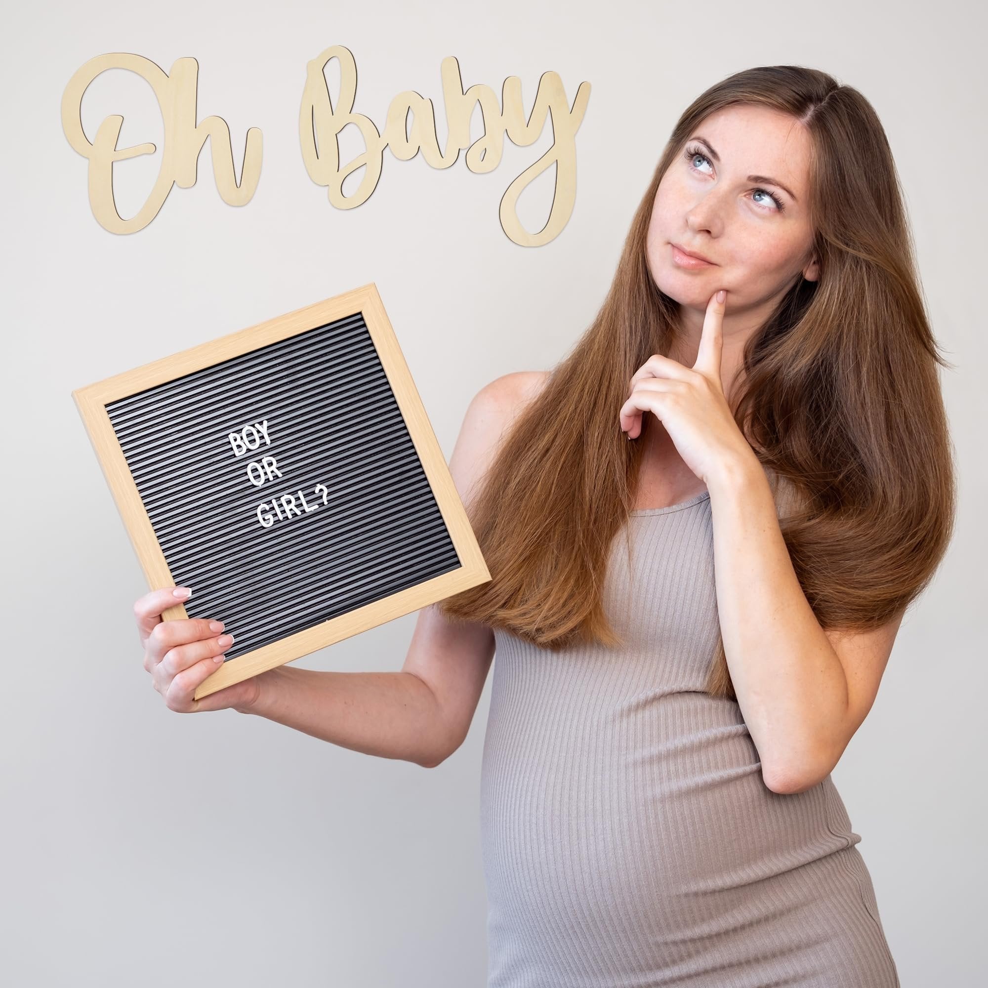 Pregnant woman holding a letter board asking 'Boy or Girl?' with wooden 'Oh Baby' sign in background