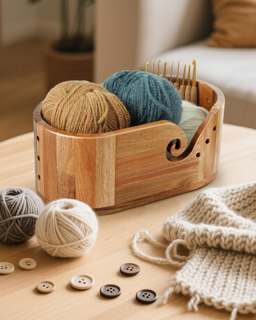 Oval wooden yarn bowl filled with yarn and crochet hooks, with yarn balls and buttons on a wooden table.