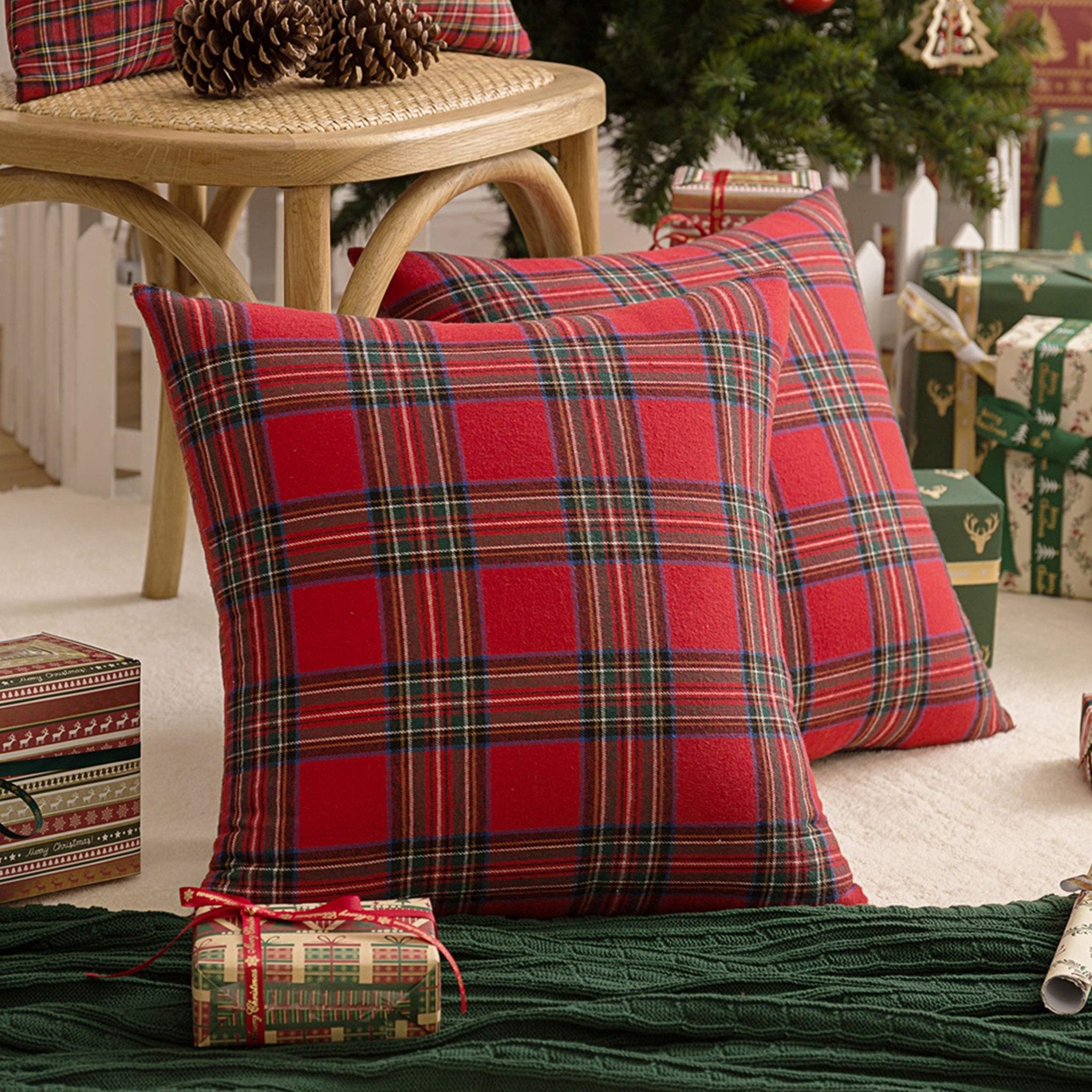 Two red plaid Christmas throw pillow covers on a rug with gifts and a tree in the background