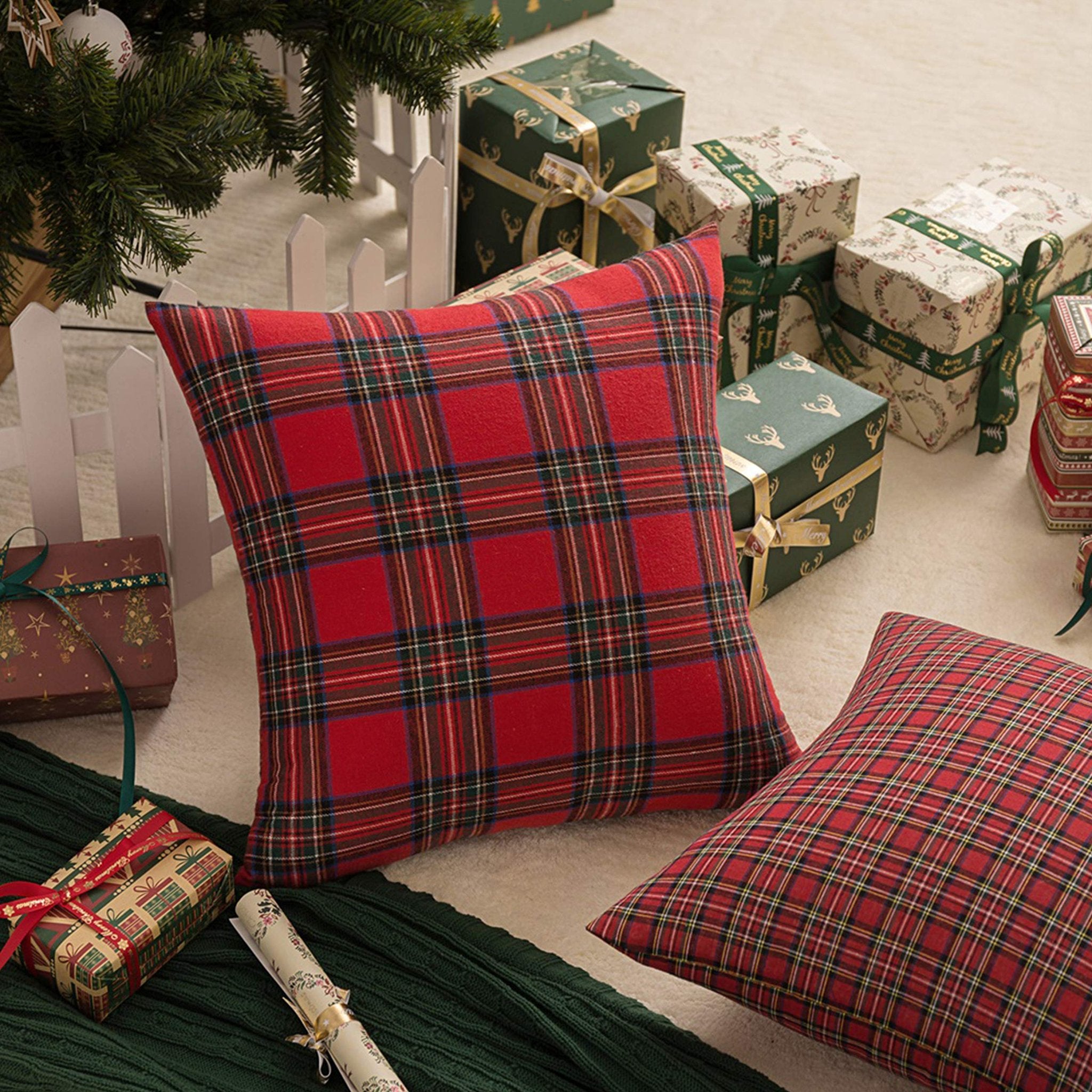 Two red and green plaid Christmas throw pillow covers arranged with gifts and a Christmas tree.