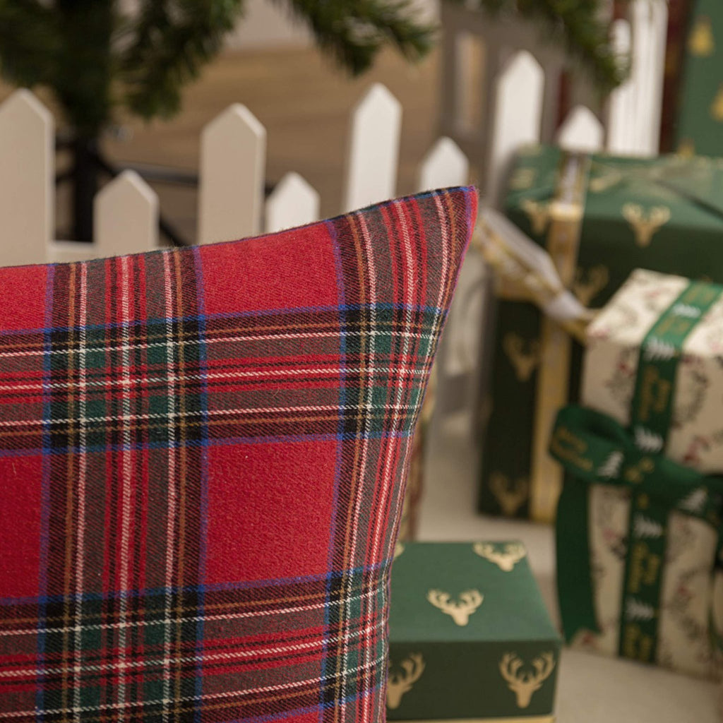 Close-up of a red and green plaid Christmas throw pillow cover with gifts and a Christmas tree in the background.
