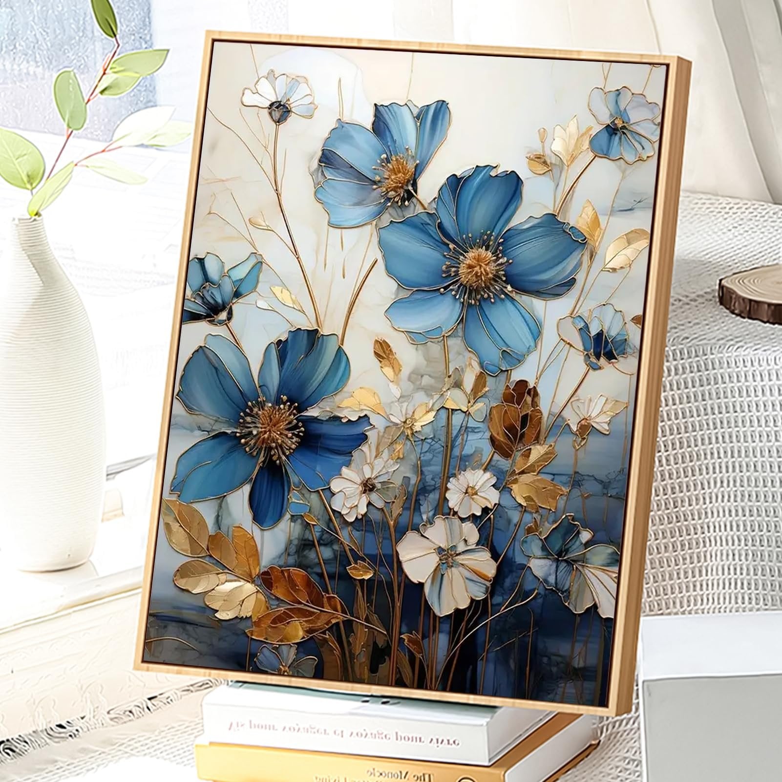 Framed paint by numbers artwork featuring blue and white flowers with gold accents, displayed on books next to a vase.