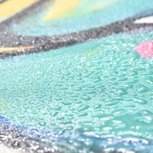 Close-up of a painted canvas with water droplets on the surface, showing teal, yellow, and pink colors.
