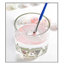 Paintbrush being dipped into water in a glass, with paint pots in the background.