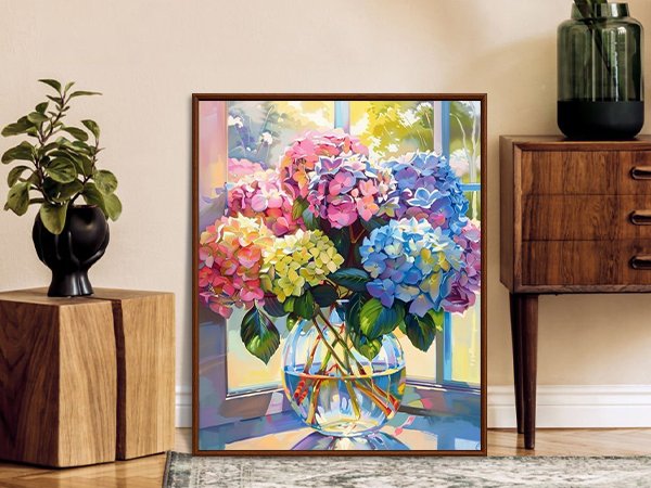 Framed painting of colorful hydrangeas in a glass vase on a windowsill, with a plant and cabinet nearby.