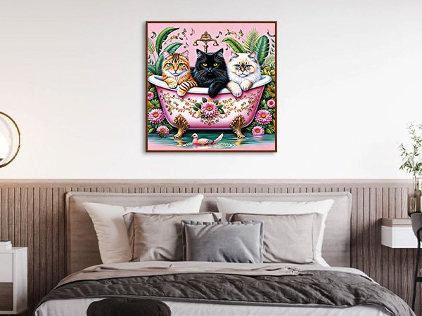 Paint by numbers artwork of three cats in a pink bathtub with flowers and a duck, displayed on a wall above a bed.