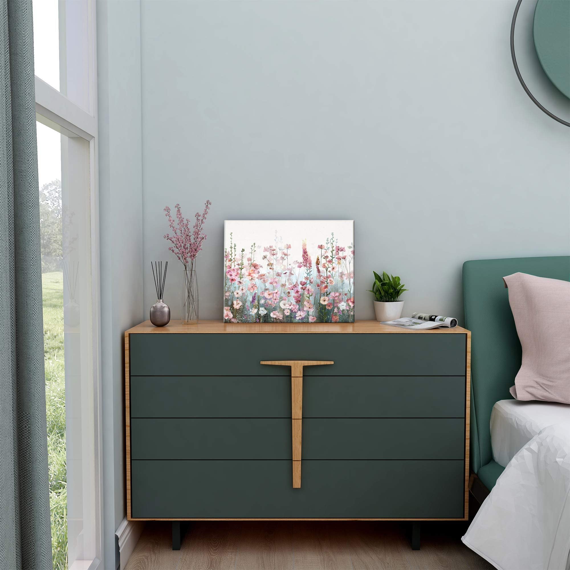 Pink wildflower floral painting displayed on a dark green dresser next to a bed