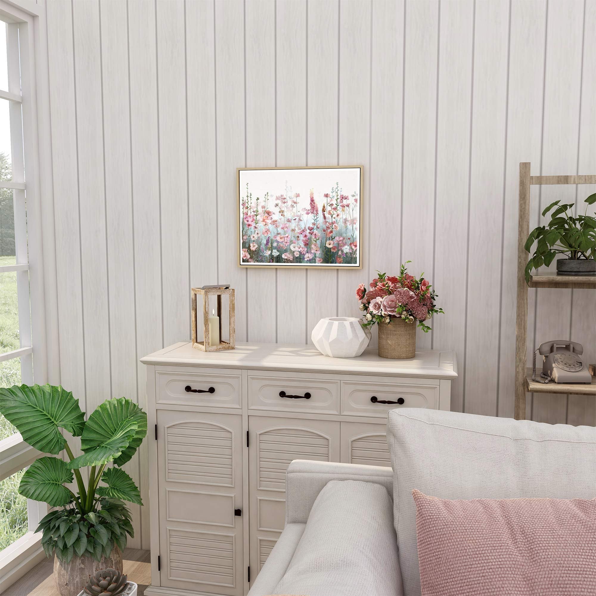Framed pink wildflower floral painting hanging above a white dresser with decorative items and plants.